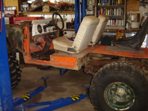 1992 Ford Bronco - An orange off-road vehicle chassis is elevated on a lift, revealing its interior and mechanical components.