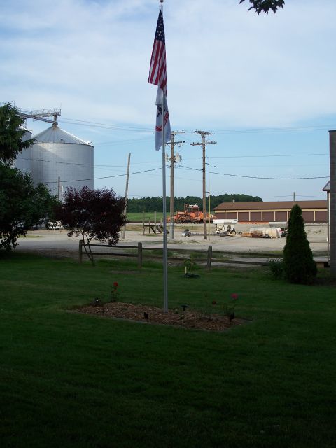 1996 Ford Bronco - A rural landscape features American and Illinois flags flying high against a partly cloudy sky, with farm structures in the background.