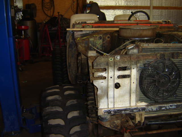 Front of a rusty Ford Bronco with engine exposed, large tires, and a fan on the radiator
