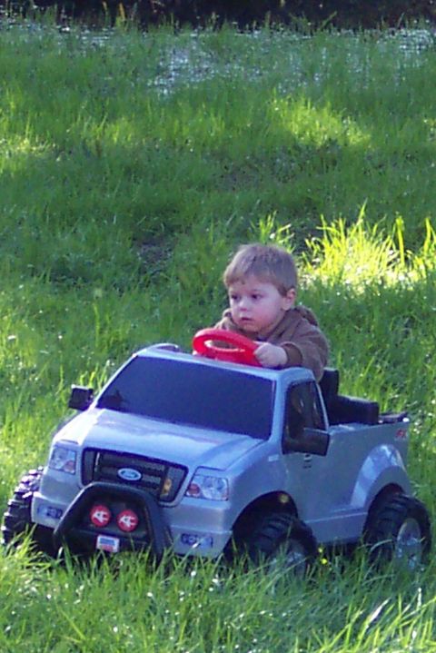 1990 Ford Bronco - Young driver takes the wheel of a toy Ford F-150 truck in a grassy field.