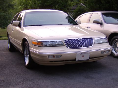 1996 Mercury Grand Marquis - A tan sedan is parked on an asphalt surface, with another vehicle partially visible to its right.