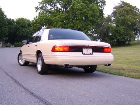 1996 Mercury Grand Marquis - Rear view of a cream-colored 1996 Mercury Grand Marquis parked on a road with trees in the background.