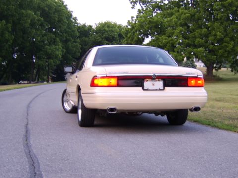 1996 Mercury Grand Marquis - Rear view of a tan sedan with chrome wheels parked on a road.