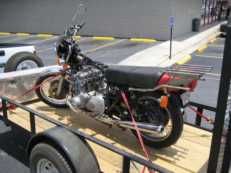 Vintage red inline-four motorcycle strapped to a wood-deck utility trailer in a parking lot