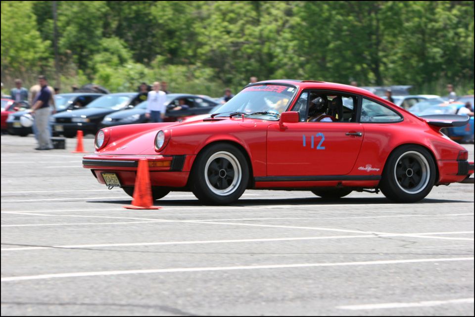 Red Porsche 911 with number 112 on door, side view, on asphalt track with orange cones