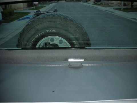 1996 Ford Bronco - Spare tire is visible through the rear window of a vehicle, with a suburban street in the background.