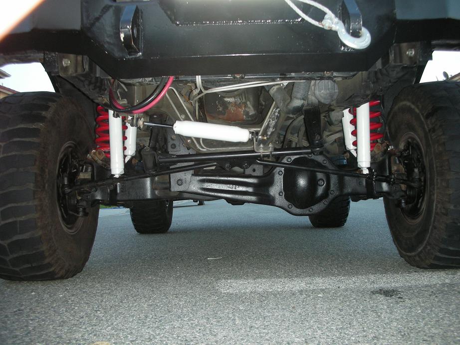 Underside view of a 4x4 vehicle's suspension and drivetrain, showing red coil springs and white shock absorbers