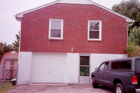 1991 Ford LTD Crown Victoria - A dark pickup truck is parked beside a brick house with a white garage door.