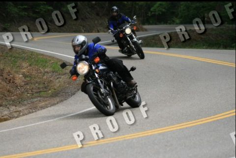 1985 Ford LTD Crown Victoria - Two motorcycles ride on a winding road, one in the foreground and another behind.