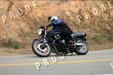1985 Ford LTD Crown Victoria - A motorcycle rider navigates a turn on a road with a rocky embankment.