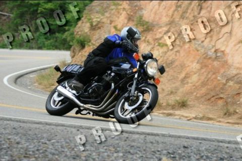 1985 Ford LTD Crown Victoria - A motorcycle rider navigates a sharp turn on a winding road with a rocky hillside.