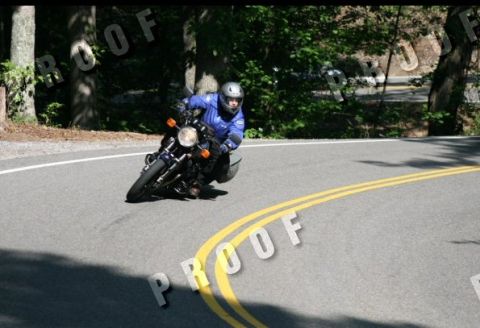 1985 Ford LTD Crown Victoria - A motorcyclist in a blue jacket and helmet navigates a sharp turn on a paved road.
