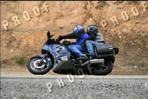 1985 Ford LTD Crown Victoria - A motorcycle carries two riders along a paved road, with a textured rock face behind them.