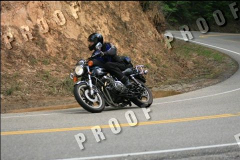 1985 Ford LTD Crown Victoria - Motorcyclist navigates a sharp turn on a scenic road.