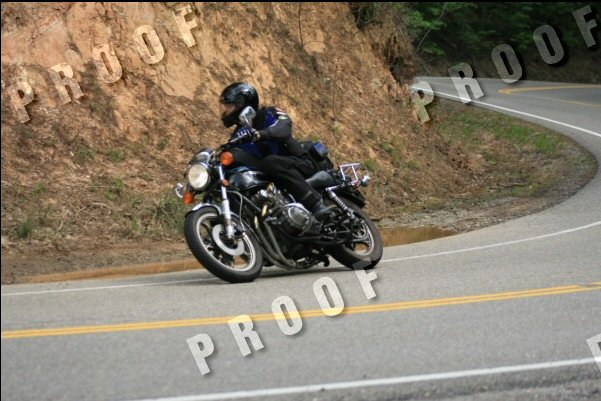 Motorcycle leaning into a curve on a paved road with a wooded hillside