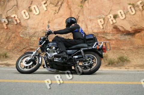 1985 Ford LTD Crown Victoria - A rider on a black motorcycle travels down a two-lane road with a rocky embankment on the side.