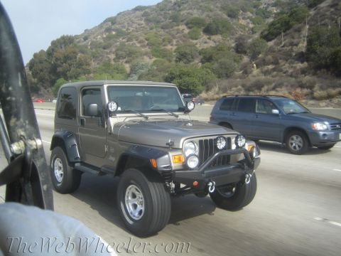 1987 Suzuki Samurai - Silver Jeep Wrangler driving on a highway with a blue SUV in the adjacent lane.