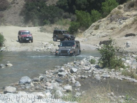 1987 Suzuki Samurai - Multiple Jeeps navigate a rocky riverbed during an off-road excursion.