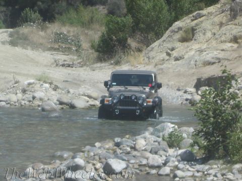 1987 Suzuki Samurai - A Jeep Wrangler navigates a shallow, rocky riverbed in a dry, hilly landscape.