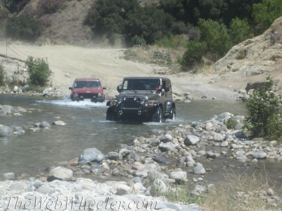 Dark gray Jeep Wrangler and red SUV crossing a stream