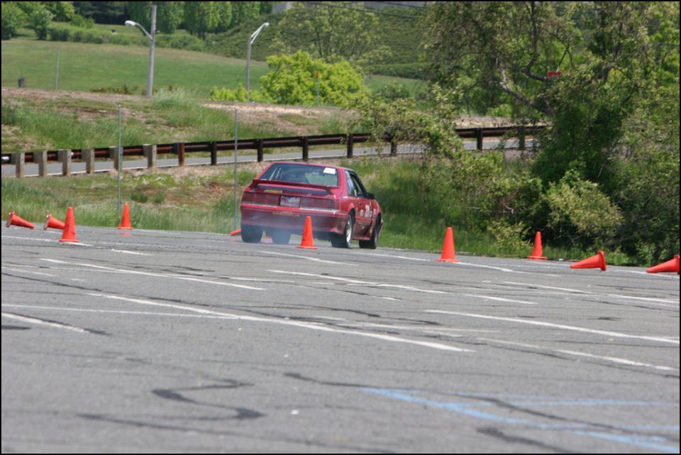 Red car with a spoiler and racing decals, viewed from the rear during an autocross event
