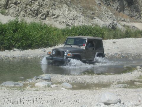 1987 Suzuki Samurai - Jeep Wrangler TJ driving through a shallow river in a rocky, natural environment.