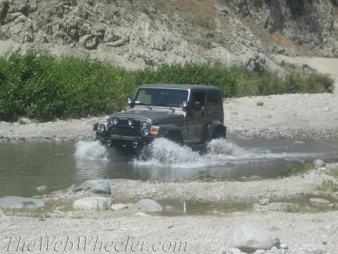 1987 Suzuki Samurai - A Jeep Wrangler navigates a shallow stream bed in a rocky, natural environment.