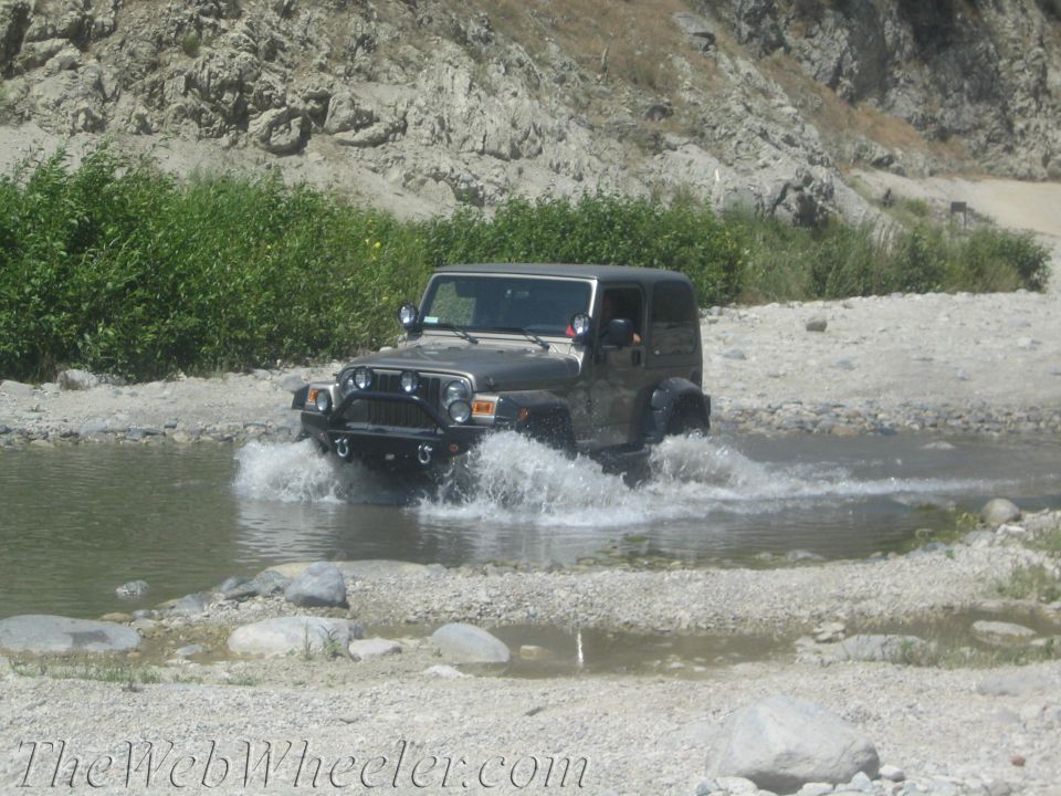 Jeep Wrangler driving through water, kicking up spray