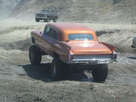 1987 Suzuki Samurai - An orange sedan with a lifted suspension and large tires navigates a muddy landscape, with another vehicle in the background.