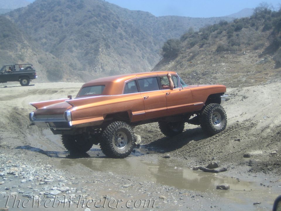Orange lifted limousine with large tires driving through mud and water