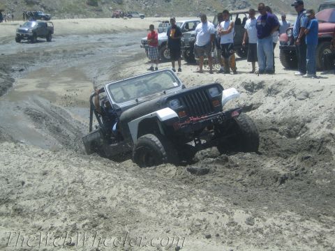 1987 Suzuki Samurai - A Jeep Wrangler TJ navigates a muddy off-road course with spectators watching.