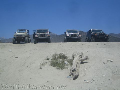 1987 Suzuki Samurai - A group of off-road vehicles are lined up on a dusty incline with mountains in the background.