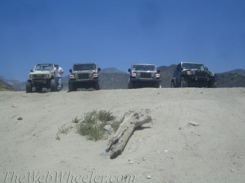 1987 Suzuki Samurai - A 1987 Suzuki Samurai and three Jeeps are parked on a dusty incline under a clear blue sky.
