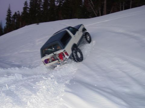 1986 Ford Bronco - A white SUV navigates a steep, snow-covered slope, leaving tracks behind.