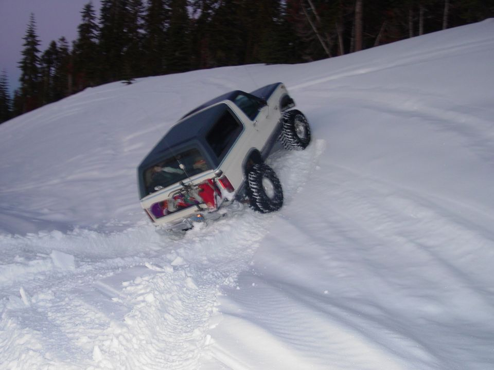 White SUV with blue top driving up a snowy hill, tires kicking up snow