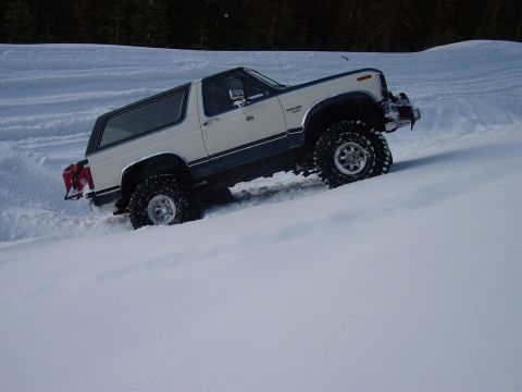 1986 Ford Bronco - A white Ford Bronco navigates a steep, snow-covered slope with aggressive off-road tires.