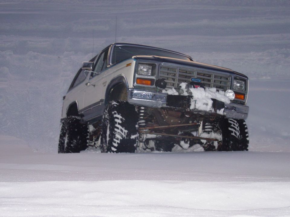 Lifted white and blue Ford Bronco on a snowbank with snow packed in the grille and bumper
