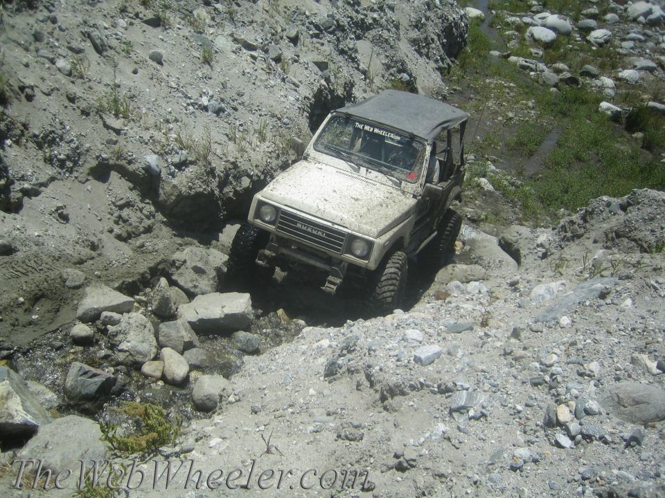 Tan Suzuki Samurai navigating a rocky, dry creek bed with a soft top