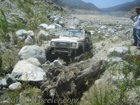 1987 Suzuki Samurai - Suzuki Samurai tackling rough terrain in a riverbed, with two people observing in the background.