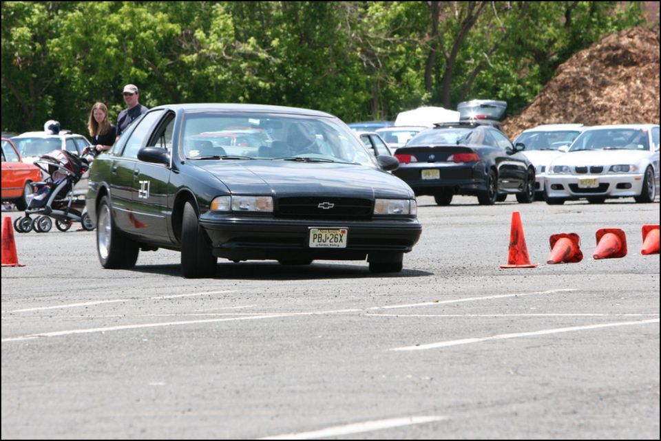 Black Chevrolet Caprice with license plate PBJ-26X driving on asphalt course