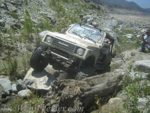 1987 Suzuki Samurai - A Suzuki Samurai navigates a rocky, off-road terrain with a driver visible inside.