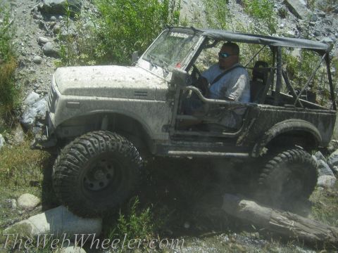 1987 Suzuki Samurai - This vehicle is navigating a challenging off-road terrain with mud and water obstacles.
