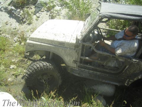 1987 Suzuki Samurai - A driver navigates a muddy trail in a white 1987 Suzuki Samurai, its body caked in dirt.