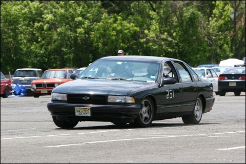 2001 Mercury Grand Marquis - A black sedan with racing numbers is seen on a track with other vehicles in the background.
