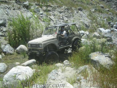 1987 Suzuki Samurai - A Suzuki Samurai tackles a challenging off-road course with large rocks and vegetation.