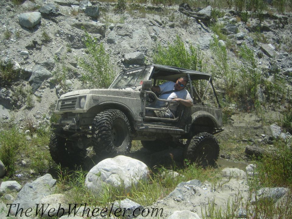 Guy driving a lifted 1987 Suzuki Samurai through a rocky stream bed