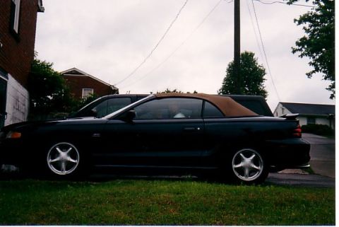 1991 Ford LTD Crown Victoria - A black convertible with a tan top is parked on grass next to another vehicle.