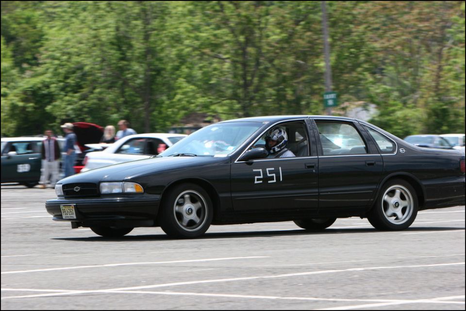 Black sedan, number 251 on door, driving on asphalt with trees in background