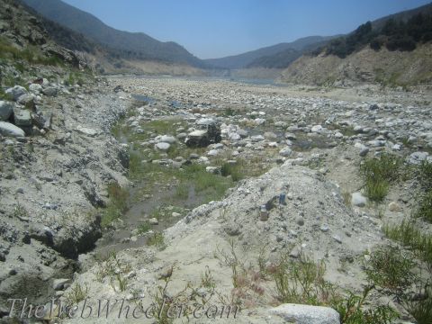1987 Suzuki Samurai - A single off-road vehicle sits in a wide, rocky riverbed under a clear blue sky.