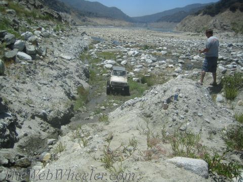 1987 Suzuki Samurai - A man watches an off-road vehicle navigate a challenging, rocky terrain in a dry riverbed.
